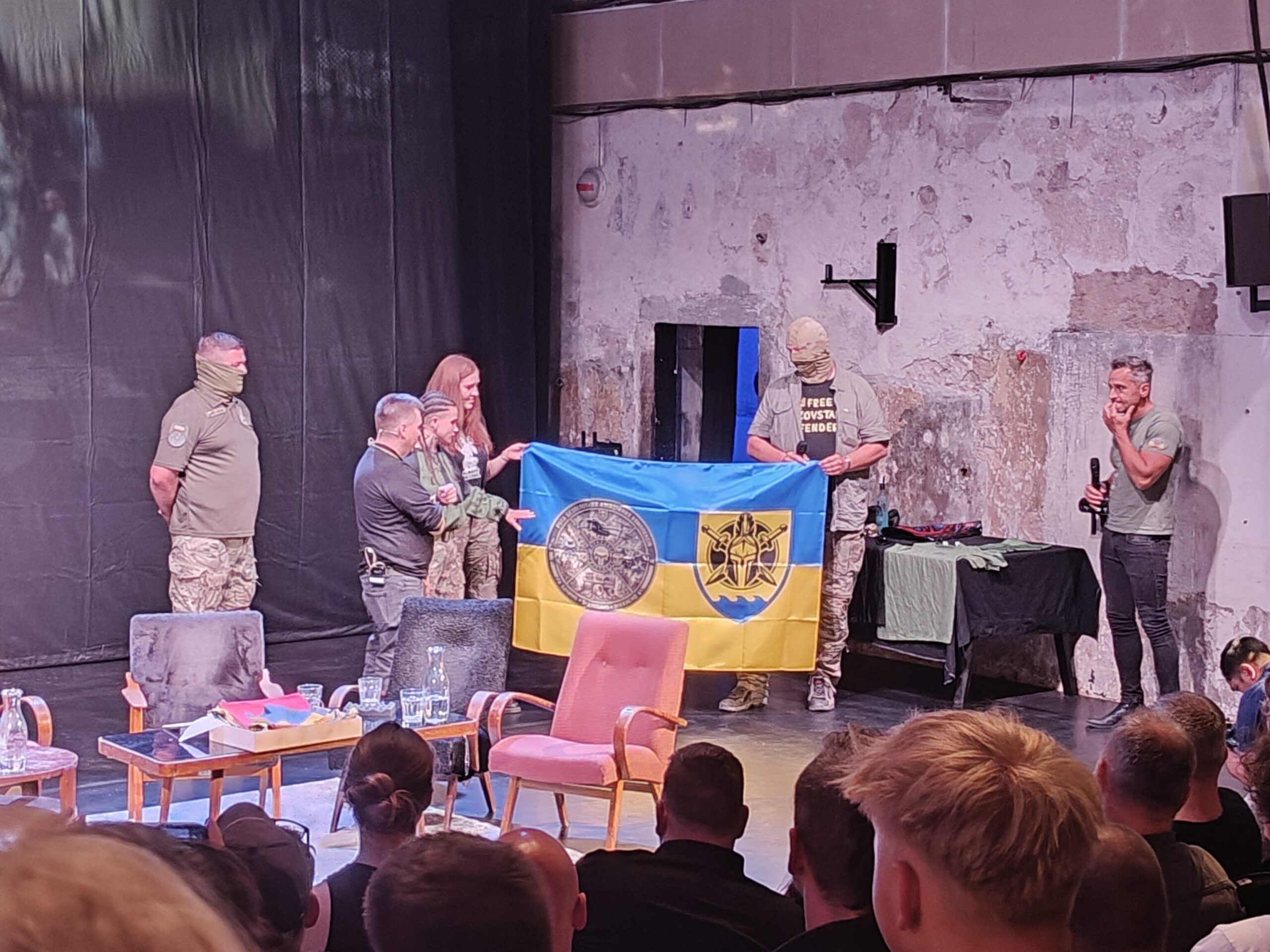 Foto z aukce. Ukrajinská vlajka s emblémy úderné roty bezpilotních letounů (vlevo) a 56. samostatné motorizované pěší brigády (vpravo)